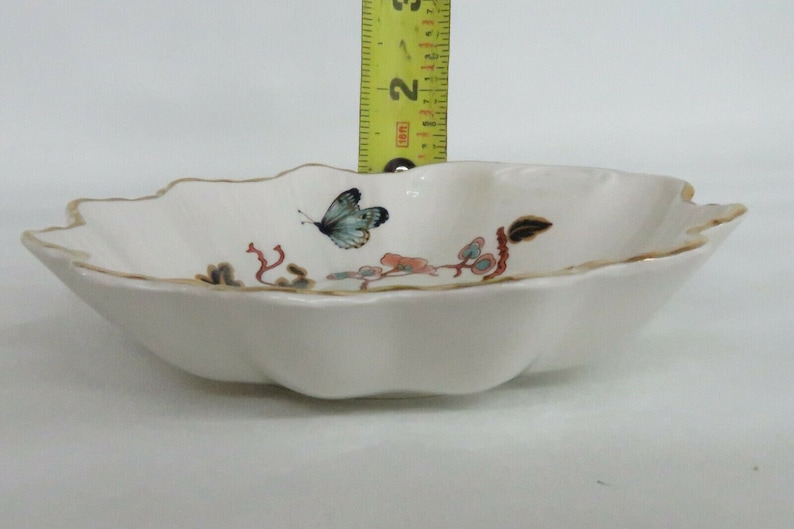 May include: A white porcelain bowl with a scalloped edge and a gold trim. The bowl features a hand-painted design of a butterfly and floral accents.