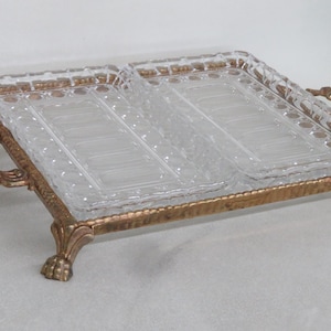 May include: A gold-toned serving tray with two clear glass divided serving dishes. The tray has ornate detailing and four feet.