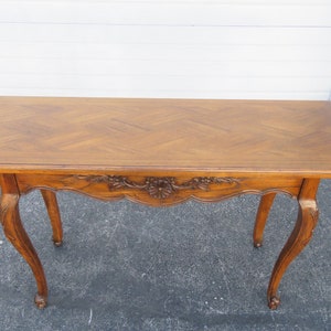 May include: A wooden console table with a parquet top and carved details. The table has a rectangular top and two curved legs on each side.