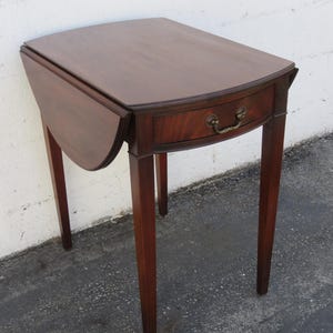 May include: A mahogany drop leaf table with a single drawer and brass hardware. The table has four legs and a rounded top.