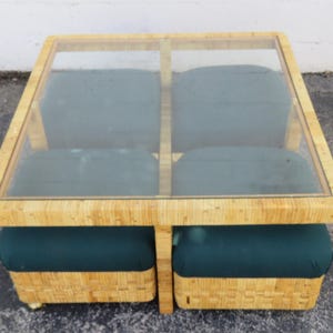 May include: Square coffee table with a clear glass top and four dark green cushions. The table has a light-colored woven base and frame. The table measures approximately 36 inches square.