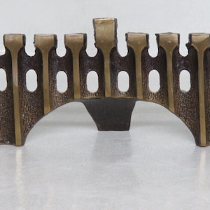 May include: A bronze menorah with a castle-like design. The menorah has nine candle holders and a central pillar.