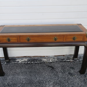 May include: A dark wood console table with three drawers and a leather top. The table has a traditional Chinese design with curved legs and brass accents.