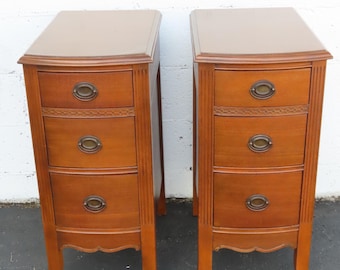 May include: A pair of matching wooden bedside tables, each featuring three stacked drawers with oval brass-toned pulls. The furniture pieces have a warm brown finish, vertical fluted detailing along the front edges, and curved apron accents.