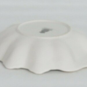 May include: White ceramic plate with a scalloped edge. The plate is empty and has a small mark on the bottom.
