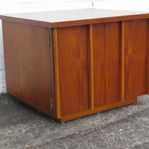 May include: A mid-century modern wooden cabinet with two doors and a top surface. The cabinet is made of dark wood with a rich grain pattern. The doors have vertical grooves and are closed.