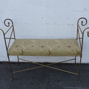 May include: A gold metal bench with a floral patterned cushion. The bench has a simple, elegant design with curved armrests.