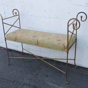 May include: A gold metal bench with a floral patterned cushion. The bench has a simple, elegant design with curved armrests.