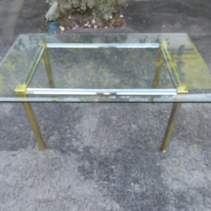 May include: A glass and brass table with a clear glass top and brass legs. The table has a simple, modern design.