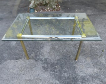 May include: A glass and brass table with a clear glass top and brass legs. The table has a simple, modern design.