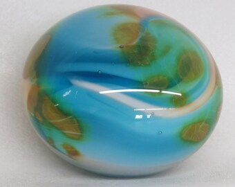 May include: A round, blue glass paperweight with white and brown swirls. The glass has a translucent quality, allowing light to pass through it.