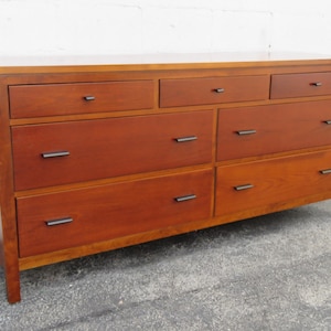 May include: A six-drawer dresser made of solid wood with a rich brown finish. The dresser has simple, rectangular drawer pulls.