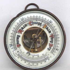 May include: A vintage round barometer with a dark metal frame and a white face. The face features a needle, temperature scales in Fahrenheit and Centigrade, and text indicating weather conditions like "Stormy" and "Fair".