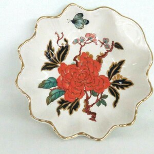 May include: A white ceramic trinket dish with a gold rim and a floral design. The design features a large red flower with green and black leaves, and a small blue butterfly.