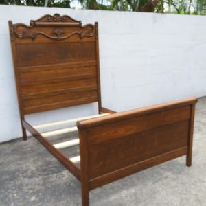 May include: A wooden bed frame with a headboard and footboard. The headboard features decorative carvings at the top. The frame is made of a dark-stained wood and has a classic design. The bed frame is designed to hold a mattress and box spring.