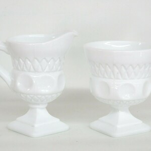 May include: A white milk glass creamer and sugar bowl set with a pedestal base and a diamond pattern.