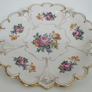 May include: A white porcelain serving platter with a scalloped edge and gold trim. The platter features a floral design with pink, orange, and yellow flowers.