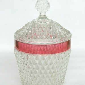 May include: A clear glass candy dish with a diamond pattern and a red band around the top. The lid has a clear glass knob.
