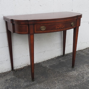 May include: A mahogany wood game table with a single drawer and a curved top. The table has a dark wood finish and is supported by four legs.