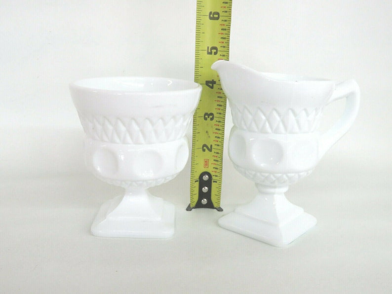 May include: White milk glass creamer and sugar bowl set with a diamond pattern and raised dots. The creamer has a handle. The sugar bowl is 3 inches tall.
