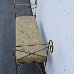 May include: A gold metal bench with a floral patterned cushion. The bench has a simple design with curved armrests and a cross-shaped frame.