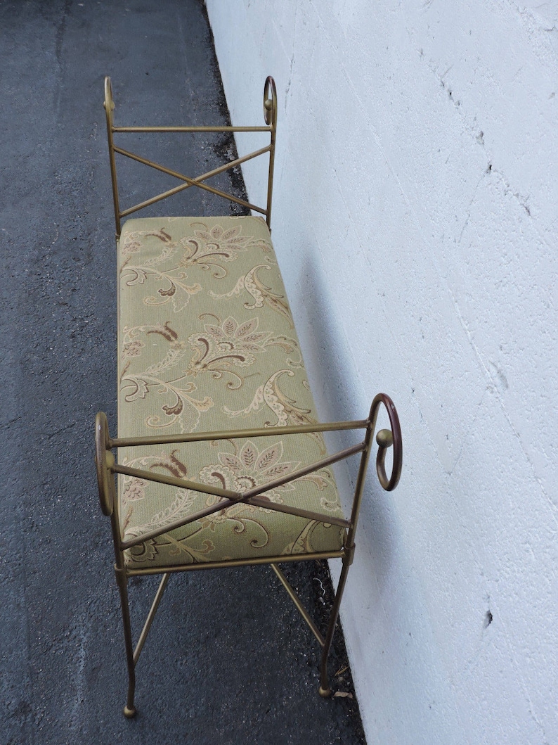 May include: A gold metal bench with a floral patterned cushion. The bench has a simple design with curved armrests and a cross-shaped frame.