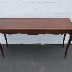 May include: A rectangular wooden console table with a smooth, polished brown surface and a thin border. The table features four slender, curved legs that flare outward, each ending in a small, metallic gold-toned foot cap at the base.