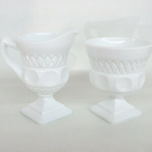 May include: A white milk glass creamer and sugar bowl set with a diamond pattern and raised dots. The set is on a white background.