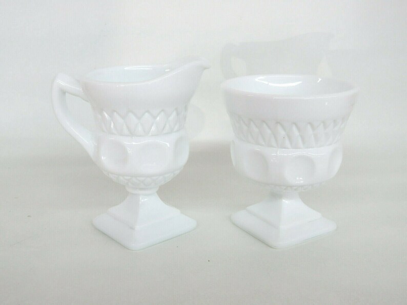 May include: A white milk glass creamer and sugar bowl set with a diamond pattern and raised dots. The set is on a white background.