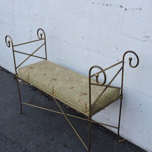 May include: A gold metal bench with a green and brown patterned cushion. The bench has a simple, elegant design with curved armrests.