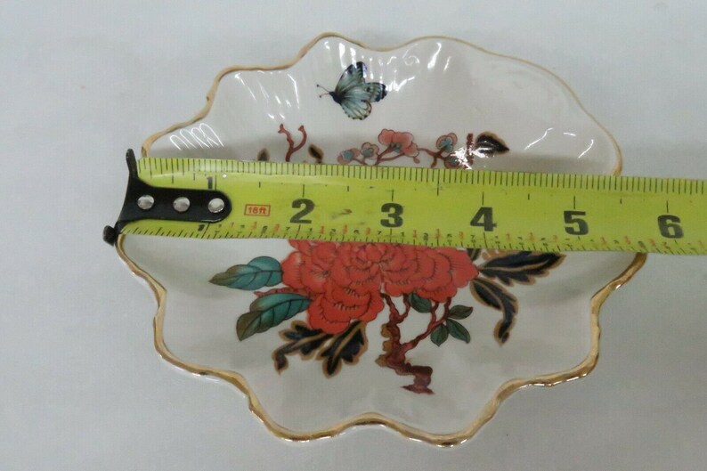 May include: A white porcelain trinket dish with a scalloped edge and a gold trim. The dish features a floral design with red, blue, and green flowers and leaves. A butterfly is painted on the dish.