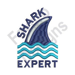 May include: Embroidered design featuring a shark fin emerging from blue waves. The text "SHARK EXPERT" is arched above the fin and below the waves. The design is in shades of blue and white on a white background.