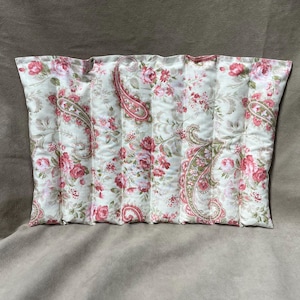 May include: A rectangular, quilted pillow with a floral pattern. The fabric features a cream background with red roses, green leaves, and paisley designs. The pillow is divided into vertical sections.