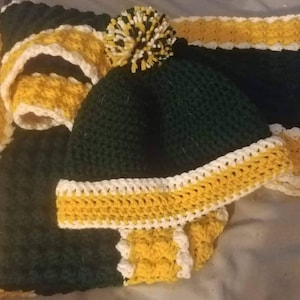 Puede incluir: Un gorro de punto verde y amarillo con un pomp&oacute;n blanco en la parte superior. El gorro tiene una franja blanca y amarilla alrededor del borde.