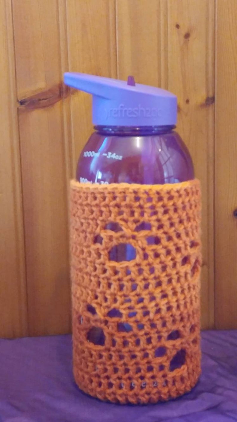 May include: A purple water bottle with a purple lid and a clear orange crocheted cover. The bottle has a label that says "refresh2go" and has markings for 1000 ml and 34 oz.