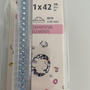 Può includere: Una confezione di Swarovski Elements, con una striscia di strass trasparenti incastonati su un supporto azzurro. La confezione contiene 42 pezzi, ciascuno di 2,80 mm. Il testo "SWAROVSKI ELEMENTS" è stampato sulla confezione.