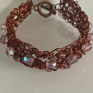 Peut inclure: Un bracelet en fil de cuivre fait à la main avec un design tissé. Le bracelet comporte des perles irisées, violet clair et un fermoir en cuivre. Ce bijou unique convient au quotidien ou aux occasions spéciales.
