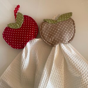 Op de afbeelding: Twee keukendoeken van stof in de vorm van een appel met witte stippen. Een doek is rood en de andere is beige.