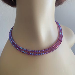Può includere: Una delicata collana a più fili con piccole perline sfaccettate nei toni del viola e del blu iridescente. La collana è esposta su un manichino, mostrando il suo design e le variazioni di colore.