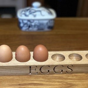 May include: A wooden egg holder with the word "EGGS" engraved on the front. The holder has 10 slots for eggs, and 5 eggs are in the holder.