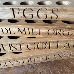 May include: A stack of four wooden egg holders with different labels. The top holder says "EGGS", the second says "HYDE MILL ORGANIC", the third says "JUST GOT LAID", and the bottom says "TILLY'S FREE RANGE EGGS".