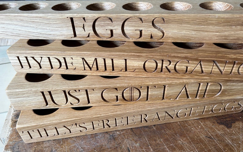 May include: A stack of four wooden egg holders with different labels. The top holder says "EGGS", the second says "HYDE MILL ORGANIC", the third says "JUST GOT LAID", and the bottom says "TILLY'S FREE RANGE EGGS".