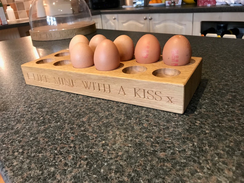 May include: A wooden egg holder with the inscription "I like mine with a kiss x" and six brown eggs inside.