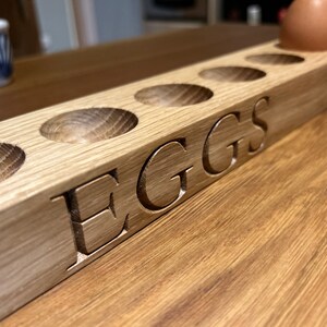 May include: A wooden egg holder with six slots and the word "EGGS" carved into the side. The holder is made of light brown wood and has a natural finish.
