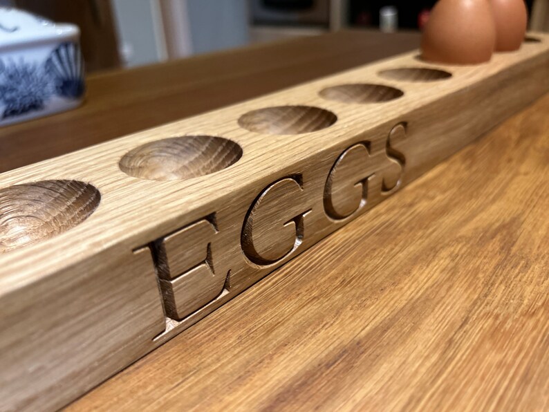 May include: A wooden egg holder with six slots and the word "EGGS" carved into the side. The holder is made of light brown wood and has a natural finish.
