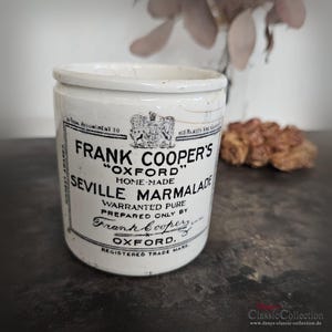 Puede incluir: Un tarro de cerámica blanco de mermelada de naranja amarga Frank Cooper's. El tarro tiene una etiqueta en blanco y negro con texto como "Oxford" y "Home-Made".