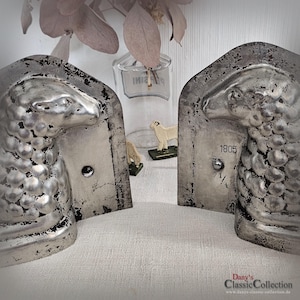 Könnte beinhalten: Zwei silberfarbene, schaförmige Buchstützen mit einem Used-Look-Finish. Auf einer Buchstütze sind die Zahl "1805" und der Bruch "2 1/4" aufgedruckt. Die Buchstützen werden auf einer weißen Oberfläche präsentiert.