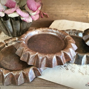 May include: A collection of antique, fluted metal tart pans with a rustic, aged appearance. The pans are arranged on a wooden surface with a vintage floral arrangement and aged paper in the background. The pans have a dark, weathered finish.