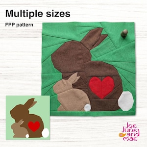 Könnte beinhalten: Ein Stoffkunstwerk mit einem braunen Hasen mit einem roten Herzen und einem kleineren beigen Hasen. Der Hintergrund ist grün mit einem geometrischen Muster. Der Text "Multiple sizes" und "FPP pattern" wird angezeigt.