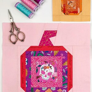 log cabin pumpkin quilt blocks in pink and orange colors on pink and orange background.log cabin pumpkin quilt block pattern in 5 different sizes, from 4x4 inch for ornaments to 6x6, 8x8, 10x10 and 12x12 inches for all sorts of amazing Halloween sewing projects. Use your favorite fabrics to fussy cut the center and turn these amazing beauties into your own pumpkin patch.